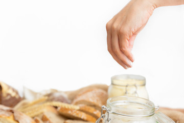 Baker taking wheat flower from jar among loafs and baguettes cut in slices. Closeup of hand, side view. Traditional bread or bakery concept