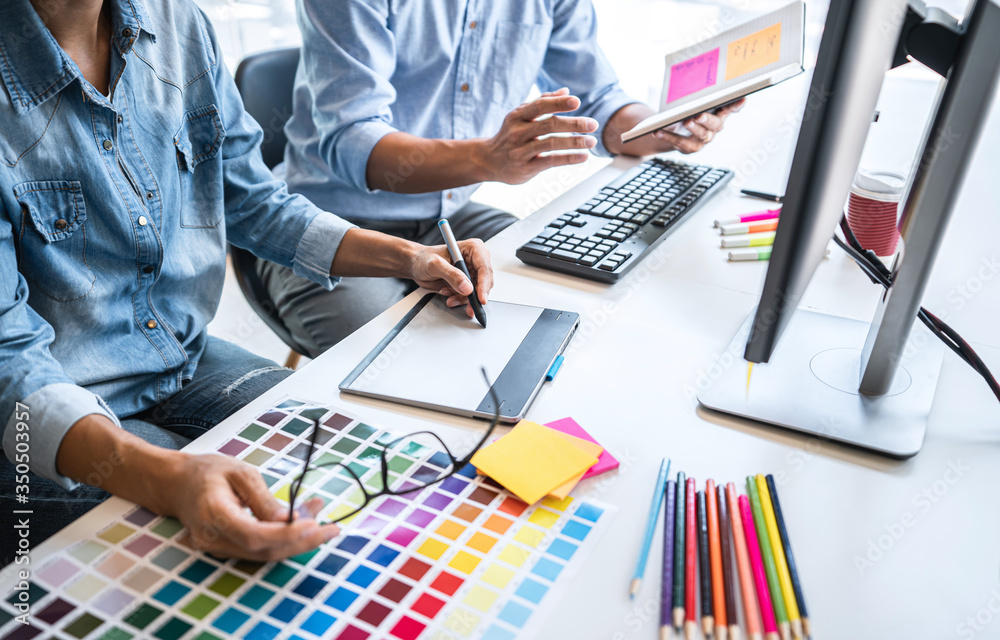 Poster Two colleague creative graphic designer working on color selection and color swatches, drawing on graphics tablet at workplace with work tools and accessories