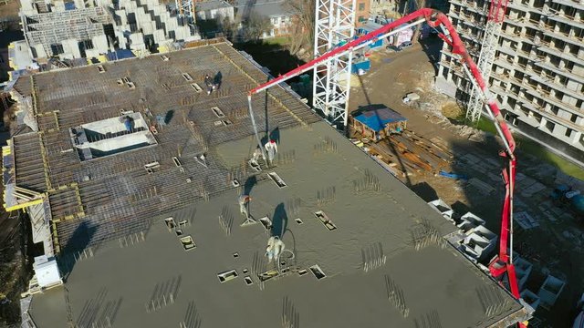 Pouring cement on the floors of residential multi-story building under construction using a concrete pump truck with high boom to supply mixture to upper floors. Aerial high top spone drone view