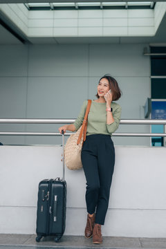 Business woman standing and using smartphone at the airport with luggage during the business trip