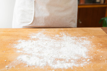 Flour spreading on wooden board for preparing dough. Unrecognizable baker in apron standing near table. Studio shot. Side view. Cooking and baking at home concept