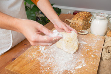 Skilled baker holding dough for pastry and dusting flour on wooden board. Fresh cereal loaf and wheat flour in glass jar. Selective focus. Studio shot. Side view. Homemade food and nutrition concept