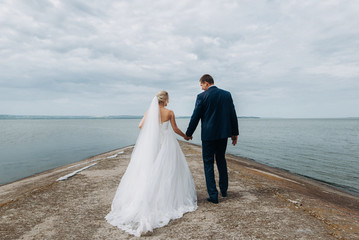 Fototapeta na wymiar Beautiful lovers newlyweds posing near sea . The bride in a luxurious dress, the groom in a stylish suit