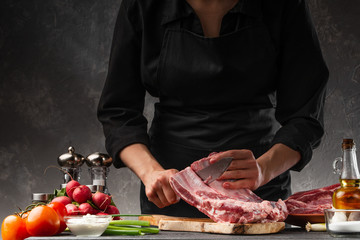 The chef cuts fresh pork ribs for cooking BBQ, on the background of vegetables. Cooking, recipe book, gastronomy. Butcher shop