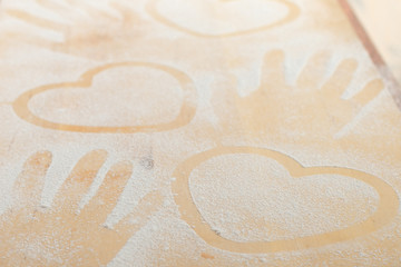 Heart and hand prints and drawing with flour on the board. Rough wooden rectangular used cutting board background with flour top view. Kitchen equipment. Concept of baking homemade,  pastry copy space