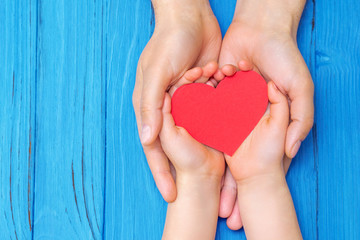 Obraz premium Top view of male and child hands holding paper red heart above wooden blue background. Concept of family and Father's day.