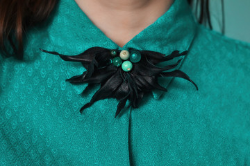 Black leather designer brooch on the collar of a girl. Close-up