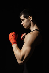 Fototapeta na wymiar Sportsman boxer practicing side kick. Red bandages on the hands. Muscular boxer on black background. Sport concept.