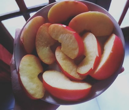 Cropped Hand Holding Sliced Apples In Bowl At Home