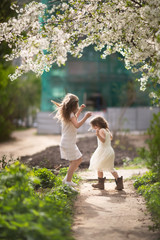 Tender young girls children jump and run near the blossoming cherry. Concept of spring, freedom and childhood. Authentic lifestyle, soft focus and sincere emotions