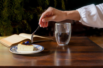 Woman hand with fork eating slice of cheesecake with cup of coffee ion the table.