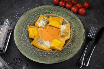 Yellow ravioli with cheese in a plate on a black background