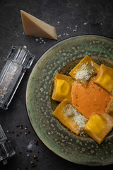 Yellow ravioli with cheese in a plate on a black background