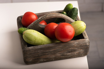 Top view of a wooden box with cucumbers, zucchini and tomatoes on a table. Healthy lifestyle, vegetarian concept