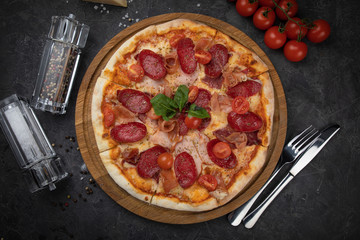 Italian pizza with tomatoes salami, parma, meat and cheese on a black background