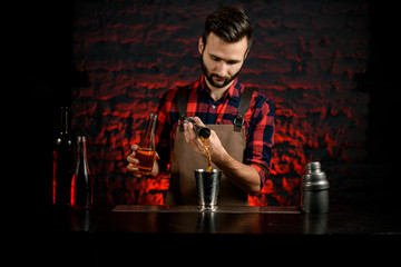 male bartender gently pours drink from jigger into glass.