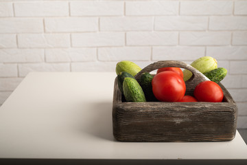 Tomatoes, zucchini and cucumbers in a wooden box on a white table. Copy space, healthy lifestyle concept