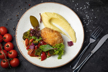 Mashed potatoes, cutlet and salad in a plate on a dark background

