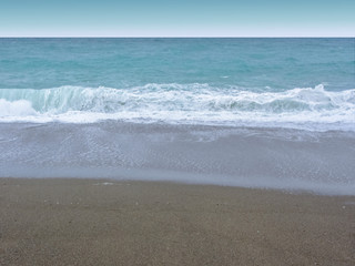 View of the blue stormy sea, white foam, waves, dark sand, empty coast.