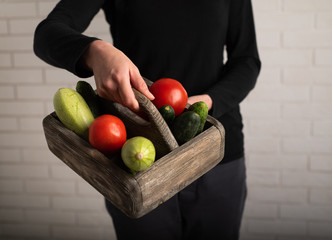 Woman holding a wooden box with donation. Tomatoes, zucchini and cucumbers in a box
