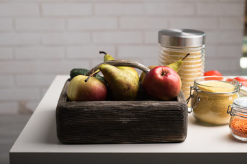Wooden box with pears, apples and vegetables, jars with wheat, lentil and couscous on a table