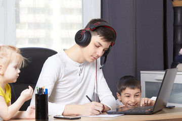 teenager looks at a laptop and writes down a task and children interfere with learning