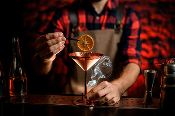 Male barman gently decorating cocktail in martini glass