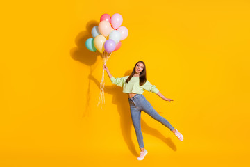 Fototapeta na wymiar Full size photo of nice carefree playful girl hold many balloons enjoy anniversary celebration wear good look clothes sneakers isolated over vivid color background