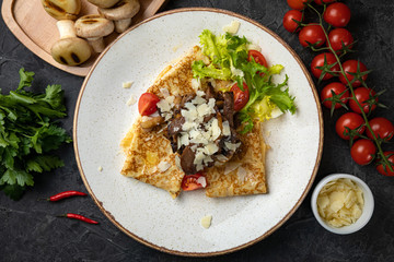 

Pancakes with mushrooms, cheese and tomatoes on a dark background