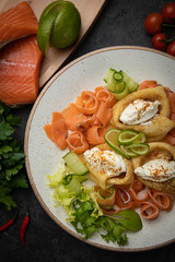 Pancakes with salmon, cheese, cucumbers and tomatoes on a dark background
