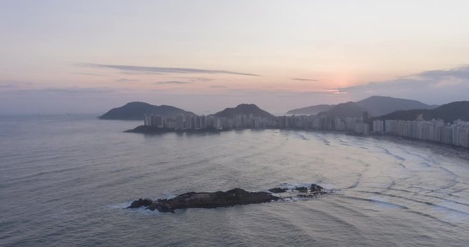 Aerial hyperlapse of sunset at beach surrounded by buildings. Waves and people moving. Pitangueiras, Guaruja, Sao Paulo, Brazil