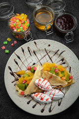 sweet pancakes with jam, honey, ice cream and candied fruit on black background	