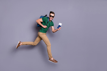 Fototapeta na wymiar Full body profile side photo of excited energetic guy jump run celebrate lucky tour victory hold visa documents wear green t-shirts pants trousers backpack isolated gray color background