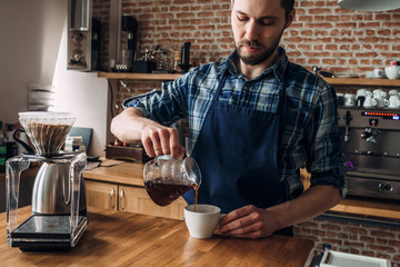 Man prepares coffee in the style of "pour over" in the barista school. Against the background of coffee equipment and a brick wall