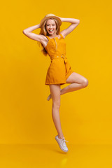 Fototapeta na wymiar Summer Fashion. Joyful Girl In Jumpsuit And Hat Jumping On Yellow Background