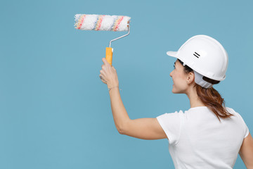 Back rear view of young woman in protective helmet hardhat hold paint roller for wall painting...