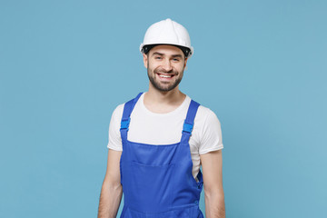 Smiling young man in coveralls protective helmet hardhat isolated on pastel blue background studio portrait. Instruments accessories for renovation apartment room. Repair home concept. Looking camera.