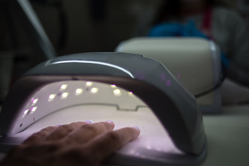 Personal care. Close up detail hand inside UV machine. Quick drying of nail paint. Professional manicure salon.