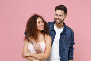 Smiling young couple two friends european guy african american girl in casual clothes isolated on pastel pink background. People lifestyle concept. Mock up copy space. Hugging, looking at each other.