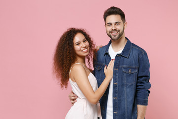 Smiling young couple two friends european guy african american girl in casual clothes isolated on pastel pink background studio. People lifestyle concept. Mock up copy space. Hugging, looking camera.