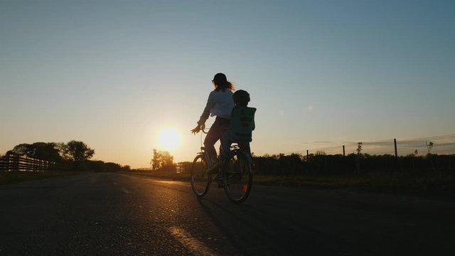 Silhouette mom with little son ride a bike on the road at sunset, slow-motion