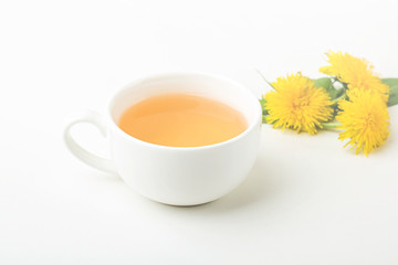 Cup of purifying, diuretic tea of dandelion with fresh leaves and flowers on a white background. Fresh spring organic herbal, green drink. Copy space for text, selective focus