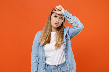 Tired exhausted young woman girl in casual denim clothes posing isolated on orange wall background studio portrait. People sincere emotions lifestyle concept. Mock up copy space. Put hand on head.