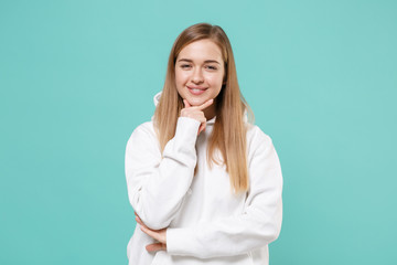 Smiling young woman girl in casual white hoodie posing isolated on blue turquoise background studio portrait. People sincere emotions lifestyle concept. Mock up copy space. Put hand prop up on chin.