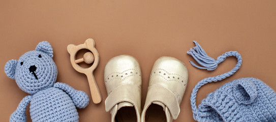 Flat lay banner with baby accessories set: crib shoes, teddy bear toy, knitted hat, wooden rattle...