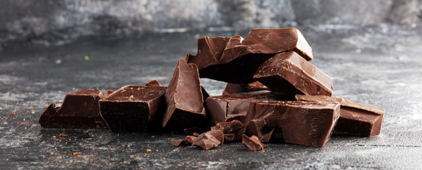 close up of bitter chocolate bars and broken piesces on rustic background.