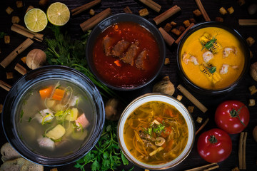 soups decorated with tomatoes, walnuts and cinnamon on a dark background: ear, borscht, cabbage soup, corn cream soup