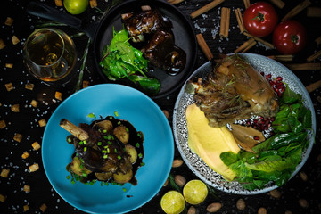pork knuckle, marble ribs, lamb leg with a side dish of potatoes, tomatoes, walnuts and cinnamon on a dark background