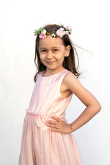 Portrait of a girl of 7 years old with brown hair and brown eyes in a gently peach dress with a wreath of flowers on her head on a white background. Spring girl. Summer time