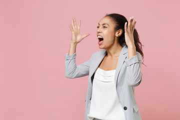 Angry irritated african american business woman in grey suit white shirt isolated on pink wall background. Achievement career wealth business concept. Spreading hands swearing screaming looking aside.